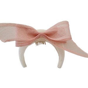 May include: A white headband with a large pink bow. The headband has a comb attached to the back.