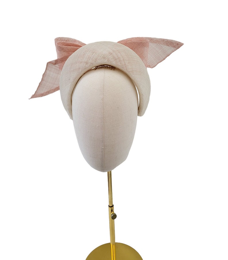 May include: A white headband with a pink bow. The headband is on a mannequin head.