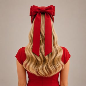 May include: A red headband featuring a large, structured bow with two long, trailing ribbons that hang down the back. The headband has a textured, lace-like pattern and is worn with a matching red short-sleeved top and long blonde wavy hair.