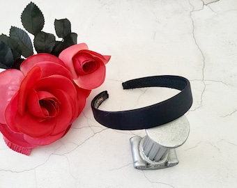 May include: A black fabric headband on a white background. The headband is on a decorative stand. Two red fabric roses are in the background.