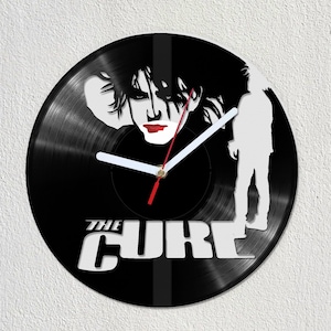 Op de afbeelding: Een zwarte vinyl platenspeler klok met een wit silhouet van Robert Smith, de zanger van The Cure, met de naam van de band in witte letters.