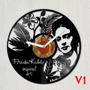 May include: Black vinyl record clock featuring a portrait of Frida Kahlo with a monkey and tropical plants. The clock face is a circular cutout with a red and yellow design. The text "Frida Kahlo inspired art" is printed below the portrait. The clock is labelled "V1" in the bottom right corner.
