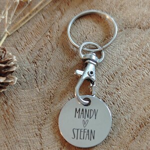 Op de afbeelding: Zilveren sleutelhanger met een rond label waarop "Mandy &hearts; Stefan" staat.
