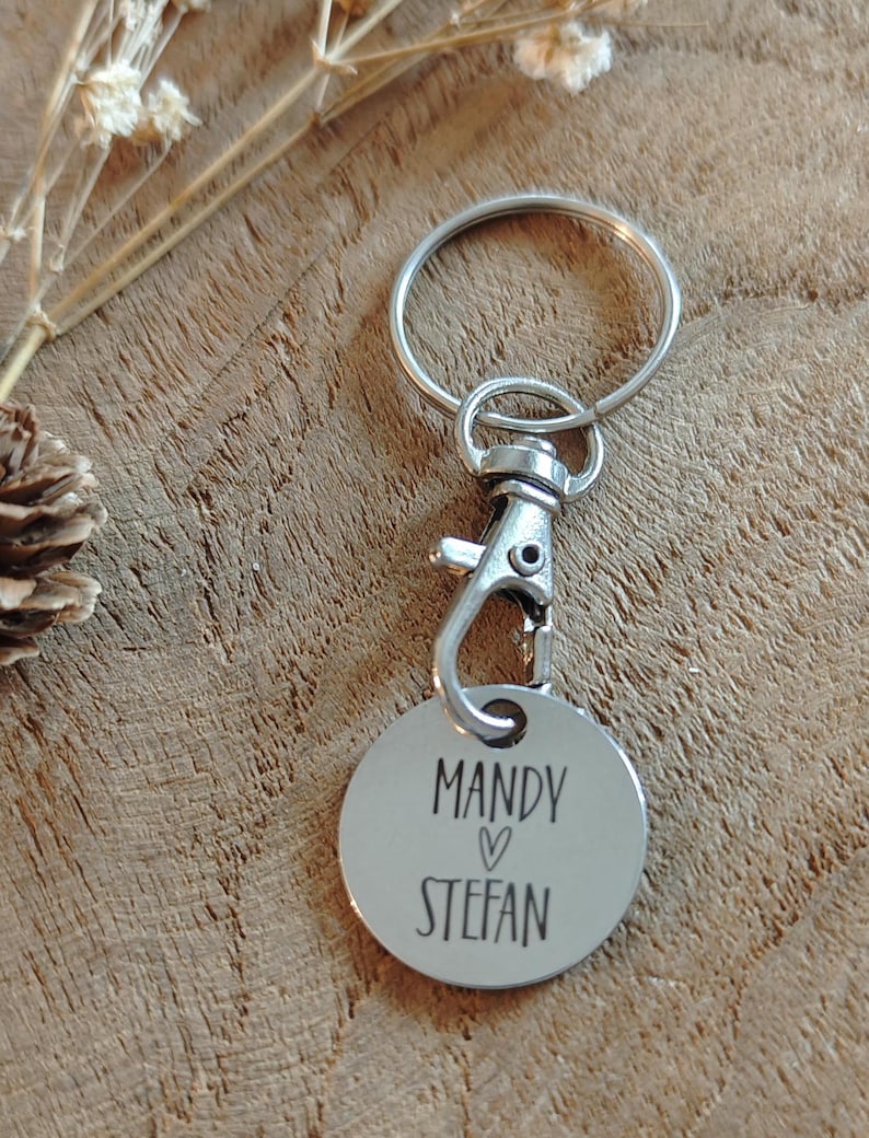 Op de afbeelding: Zilveren sleutelhanger met een rond label waarop "Mandy &hearts; Stefan" staat.