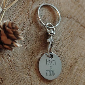 Op de afbeelding: Zilveren sleutelhanger met een rond label waarop "Mandy &hearts; Stefan" staat.
