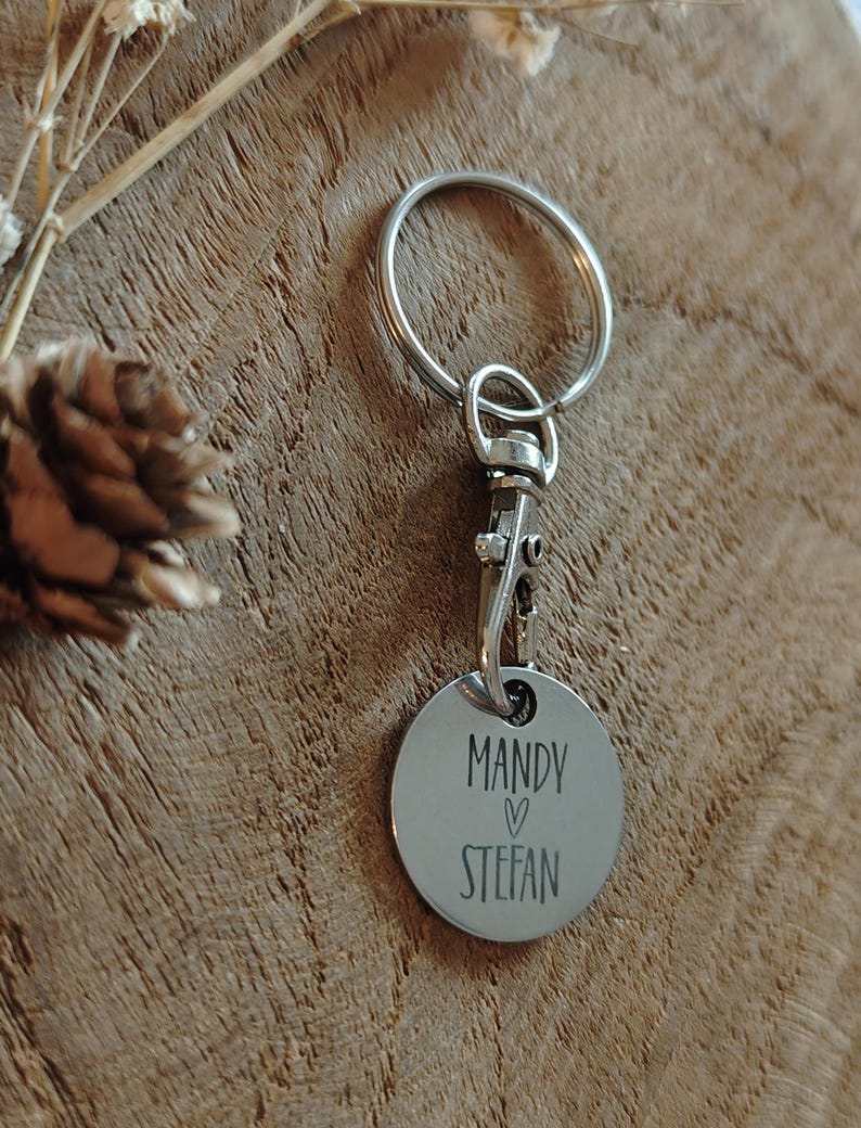 Op de afbeelding: Zilveren sleutelhanger met een rond label waarop "Mandy &hearts; Stefan" staat.