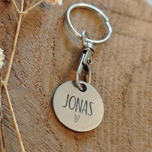 May include: Silver keychain with a round tag that says "JONAS" with a small heart symbol.