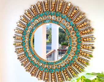 May include: A large, round, gold-framed mirror with a sunburst design. The mirror is decorated with turquoise and white tiles in a geometric pattern.