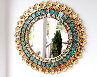 May include: A round mirror with a gold frame decorated with turquoise and white floral tiles. The mirror is hanging on a white wall.