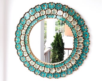 May include: A round mirror with a decorative frame made of turquoise and white tiles with gold accents. The tiles are arranged in a circular pattern and feature floral designs.