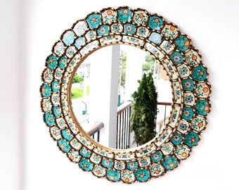 May include: A round mirror with a decorative frame made of turquoise and white tiles with gold accents. The tiles have a floral pattern.