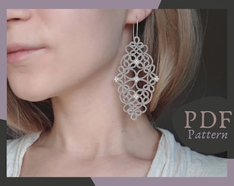 May include: Silver earrings with a delicate, intricate design featuring small white beads. The earrings are in the shape of a teardrop and have a PDF pattern.