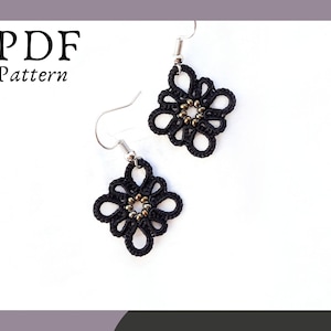 Może przedstawiać: Para czarnych, szydełkowych kolczyków z złotymi koralikami w środku. Kolczyki wiszą na srebrnych haczykach.