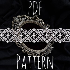 Pode incluir: Um close-up de uma delicada renda branca com um padr&atilde;o floral, exibida em um fundo de tecido preto com uma moldura de prata ornamentada. O texto "PDF PATTERN" est&aacute; escrito abaixo da moldura.