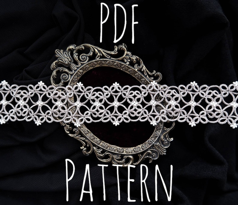 Pode incluir: Um close-up de uma delicada renda branca com um padr&atilde;o floral, exibida em um fundo de tecido preto com uma moldura de prata ornamentada. O texto "PDF PATTERN" est&aacute; escrito abaixo da moldura.