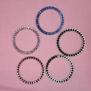 May include: Five different colored rhinestone-encrusted metal rings. The rings are all the same size and shape, but have different colored rhinestones. The colors are pink, blue, black, green, and red.