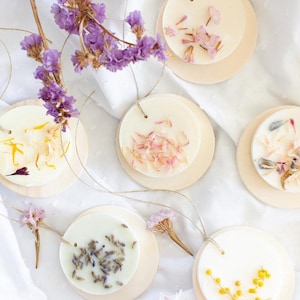 Puede incluir: Seis fundidos de cera redondos, blancos y perfumados con flores secas prensadas en la cera. Los fundidos de cera están unidos a círculos de madera con un cordel.