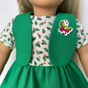 May include: A green dress with a white holly print top and a green vest. The dress has a candy cane and holly pin.