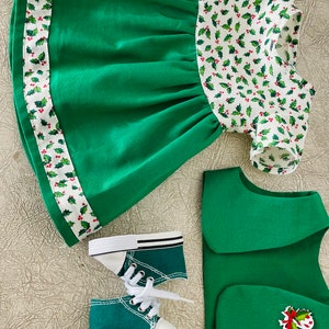 May include: A green and white Christmas-themed dress with a holly pattern, a green vest with a holly and candy cane applique, and a pair of green canvas sneakers with white laces.