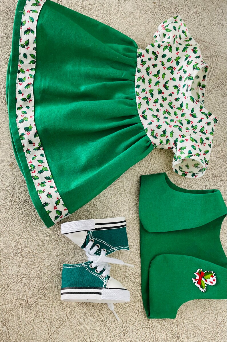May include: A green and white Christmas-themed dress with a holly pattern, a green vest with a holly and candy cane applique, and a pair of green canvas sneakers with white laces.