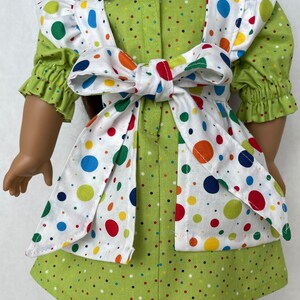 May include: A green and white polka dot dress with a white apron featuring colourful polka dots. The apron has a white bow tied at the back.