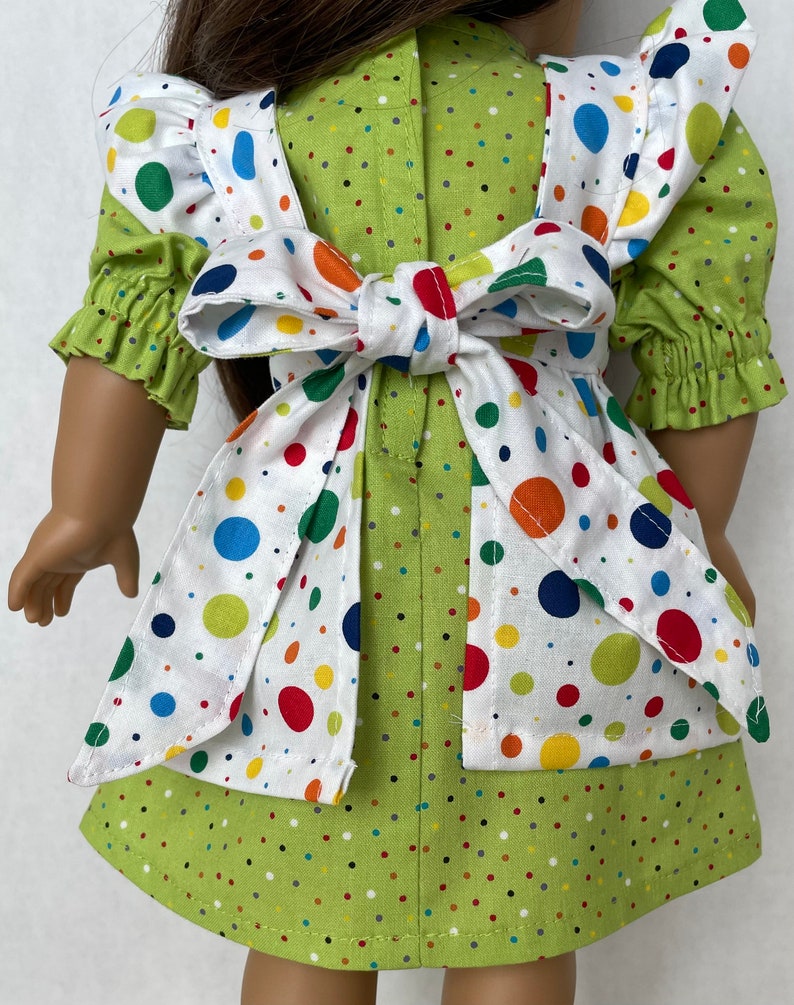 May include: A green and white polka dot dress with a white apron featuring colourful polka dots. The apron has a white bow tied at the back.