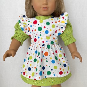 May include: A white dress with a green bodice and colourful polka dots. The dress has a ruffled neckline and green sleeves.