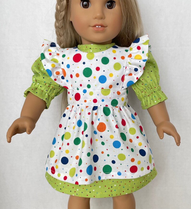 May include: A white dress with a green bodice and colourful polka dots. The dress has a ruffled neckline and green sleeves.