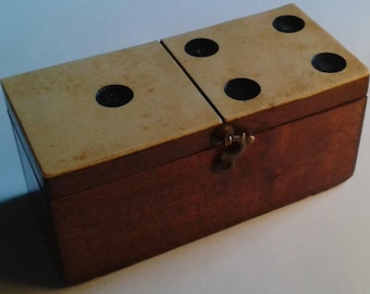 May include: A vintage domino set in a wooden box. The box is rectangular with a hinged lid and a brass clasp. The dominoes are cream-colored with black dots. The box is made of dark brown wood.