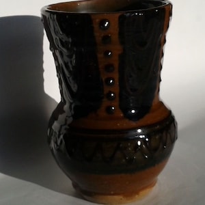 May include: A brown and black ceramic vase with a geometric design. The vase has a wide base and a narrow neck.