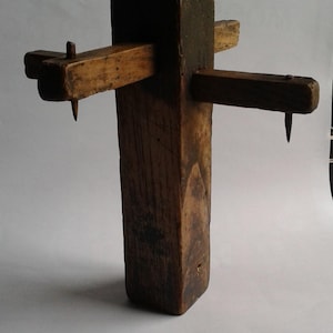Könnte beinhalten: Ein verwittertes Holz-Anreißmaß mit einem vertikalen Pfosten und zwei horizontalen Armen. Jeder Arm hat einen Metallstift. Das Holz hat ein dunkles, gealtertes Aussehen, was auf ein antikes Holzbearbeitungswerkzeug hindeutet.