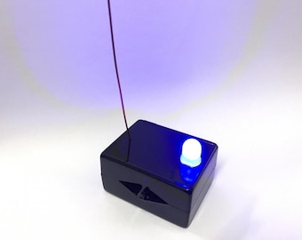 May include: A small, black box with a white LED light on top. A thin red wire extends from the box.