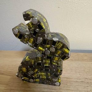 K&ouml;nnte beinhalten: Eine transparente Harzskulptur in Form eines Hasen, gef&uuml;llt mit kleinen, gelben, schwarzen und silbernen elektronischen Bauteilen. Die Skulptur steht auf einer Holzoberfl&auml;che. Einzigartiges Dekorationsst&uuml;ck.