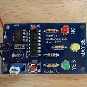 May include: A blue printed circuit board electronic decision maker kit with a red, yellow, and green LED light array labeled NO, MAYBE, and YES. The board features a red push button, resistors, capacitors, and text reading NightFire Electronics, LLC.