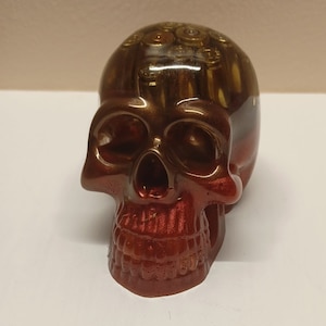 May include: A red and gold resin skull sculpture with bullet casings embedded in the top of the head.