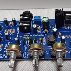 May include: A blue circuit board with a 32W guitar amplifier module. The board has three knobs, a black heatsink, and a black input jack. The text "NightFire Electronics LLC" and "Copyright 2025 Ocala, FL" is printed on the board.