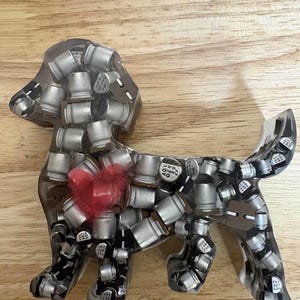 May include: A clear resin dog figurine filled with silver electronic components. A red heart is embedded in the center of the dog's body. The figurine is displayed on a wooden surface.