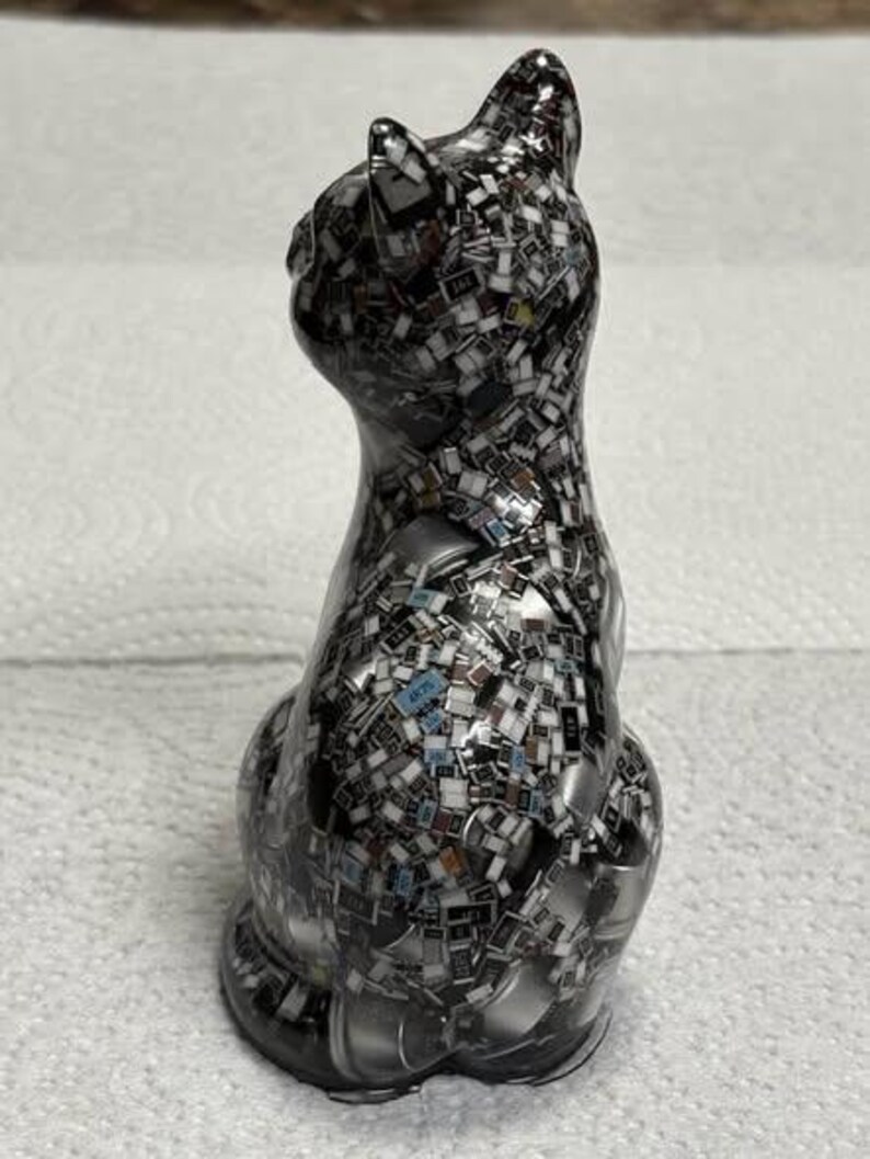 Puede incluir: Figura decorativa de gato con un patr&oacute;n de mosaico de peque&ntilde;as piezas rectangulares en tonos negro, blanco y gris. El gato est&aacute; sentado, con la cabeza ligeramente girada hacia un lado. La figura tiene un acabado brillante.