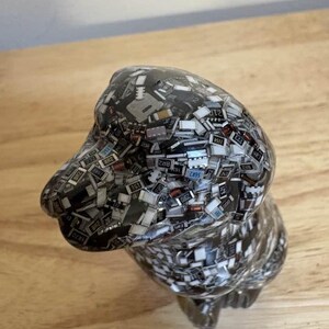 May include: A handcrafted dog figurine, composed of small, rectangular electronic components. The sculpture is primarily dark gray with a glossy finish, and the components have various colors and markings. The dog is posed in a seated position.