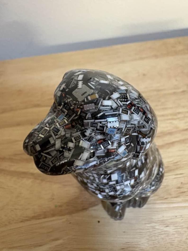 May include: A handcrafted dog figurine, composed of small, rectangular electronic components. The sculpture is primarily dark gray with a glossy finish, and the components have various colors and markings. The dog is posed in a seated position.