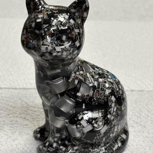 Puede incluir: Figura decorativa de gato con un patr&oacute;n de mosaico. El gato es principalmente negro con una mezcla de plata, blanco y otros colores. La figura est&aacute; sentada con las orejas erguidas.