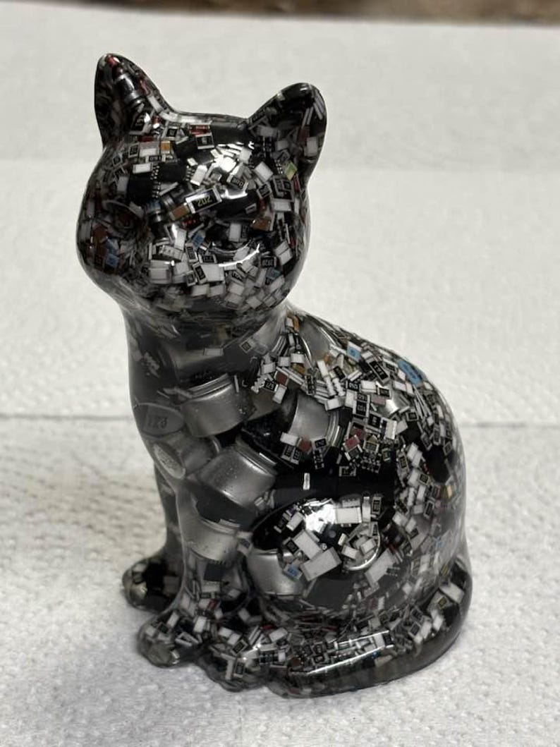 Puede incluir: Figura decorativa de gato con un patr&oacute;n de mosaico. El gato es principalmente negro con una mezcla de plata, blanco y otros colores. La figura est&aacute; sentada con las orejas erguidas.