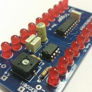 May include: A blue circuit board with a red LED light strip, a black rotary switch, and a small integrated circuit. The board has text that reads "Trigger", "Output", "5V", "AAU", and "July 2009".