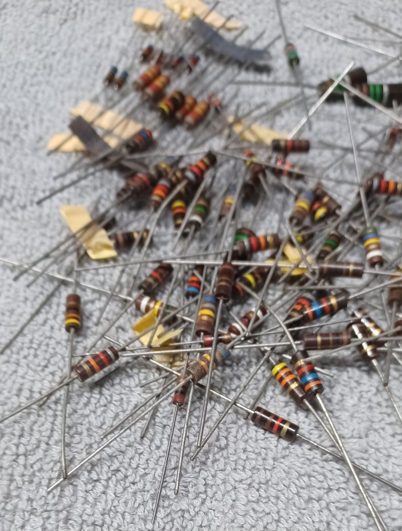 Op de afbeelding: Een grote stapel verschillende elektronische weerstanden met gekleurde banden. De weerstanden zijn willekeurig gerangschikt op een grijs oppervlak.