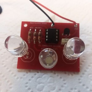 May include: A red circuit board with three clear LED lights, a black integrated circuit chip, and three resistors. The board has the text "LED DRIVER" and "PROTOTYPE BOARD" printed on it.