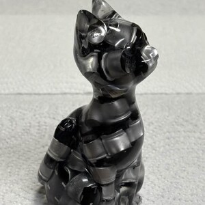 Puede incluir: Una figura de gato gris transparente con un patr&oacute;n de rayas. El gato est&aacute; sentado, con las orejas erguidas. La figura est&aacute; hecha de un material transparente, que permite el paso de la luz.