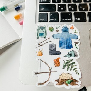 K&ouml;nnte beinhalten: Eine Sammlung von Aquarell-Aufklebern mit Camping- und Outdoor-Motiven. Enth&auml;lt einen blauen Rucksack, einen blauen Regenmantel, ein Lagerfeuer, Pfeil und Bogen, ein Eichh&ouml;rnchen, einen Stiefel, eine M&uuml;tze und einen Baumstumpf.