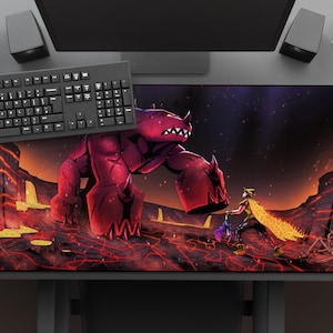 May include: A large rectangular mouse pad featuring a fantasy scene with a giant red monster and a warrior. The pad has a black border and is surrounded by a keyboard, mouse, and other desk accessories.