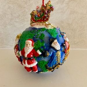 May include: A Christmas ornament shaped like a globe, featuring Santa Claus and other figures. The ornament has a red ribbon for hanging and the words "Christmas to All". The globe is blue and green with painted details.