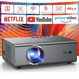 Op de afbeelding: Een grijze rechthoekige projector met een prominente lens aan de voorzijde. Daarboven toont een display iconen voor Dolby, Auto Focus, WiFi 6, Bluetooth 5.3, Auto Keystone en DTS X, naast de logo's van Netflix, YouTube en Prime Video.